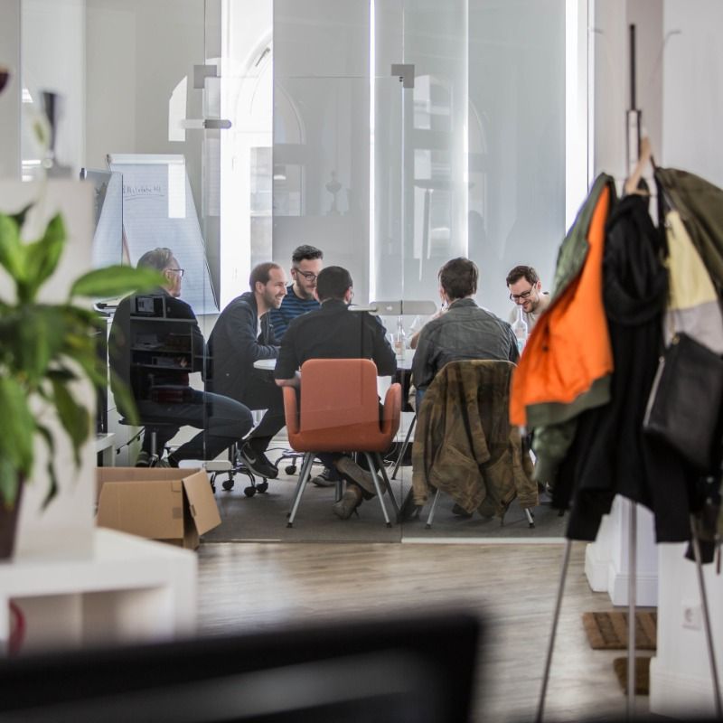 Kollegen der Logic Joe Group besprechen sich am Tisch hinter der Glaswand im hellen Altbau-Büro