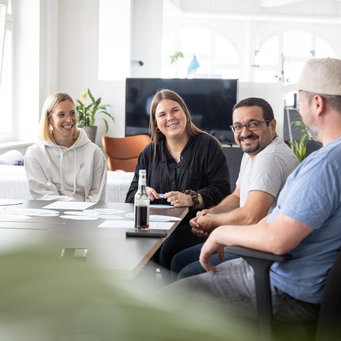 Vier Kollegen sitzen lachend am Workshop-Tisch mit Moderationskarten